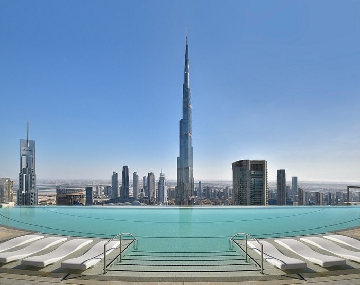 Hotel with Burj Khalifa view, infinity pool overlooking a cityscape with surrounding skyscrapers under a clear blue sky.