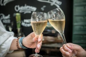 Two people toasting champagne glasses in front of a chalkboard.