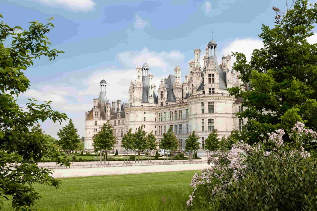 A large castle in the middle of a grassy field located in one of the French wine regions.