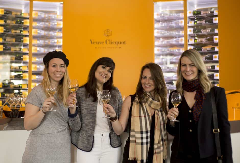 A group of women holding wine glasses in front of a yellow wall.