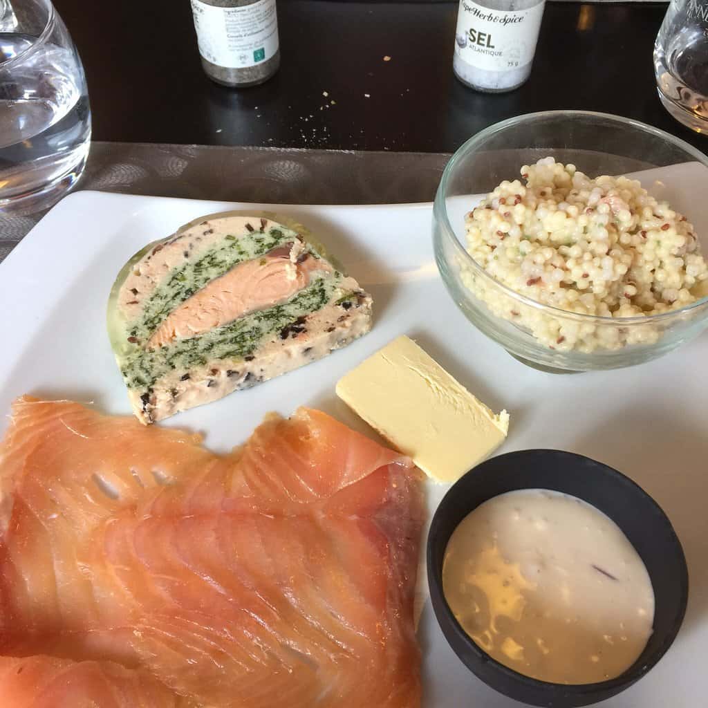 A delicious meal of salmon and bread served on a white plate accompanied by a bowl of hummus at a restaurant in Reims.