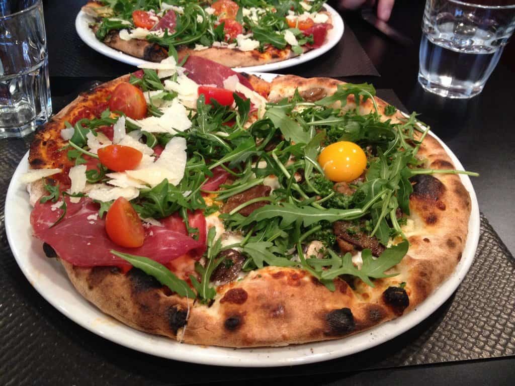 A pizza on a plate with arugula and tomatoes served at a restaurant in Reims.