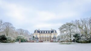 A large mansion in the snow with trees in the background.