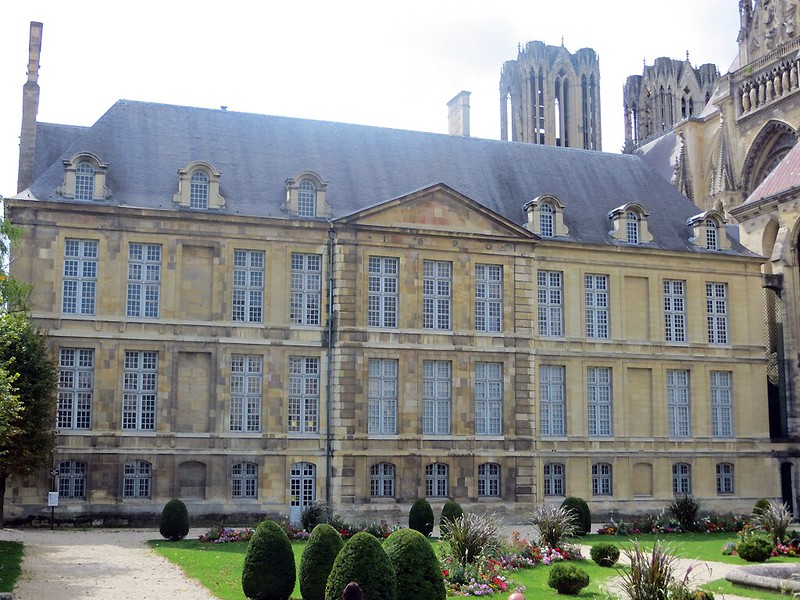 A large stone building with a Reims garden in front of it.