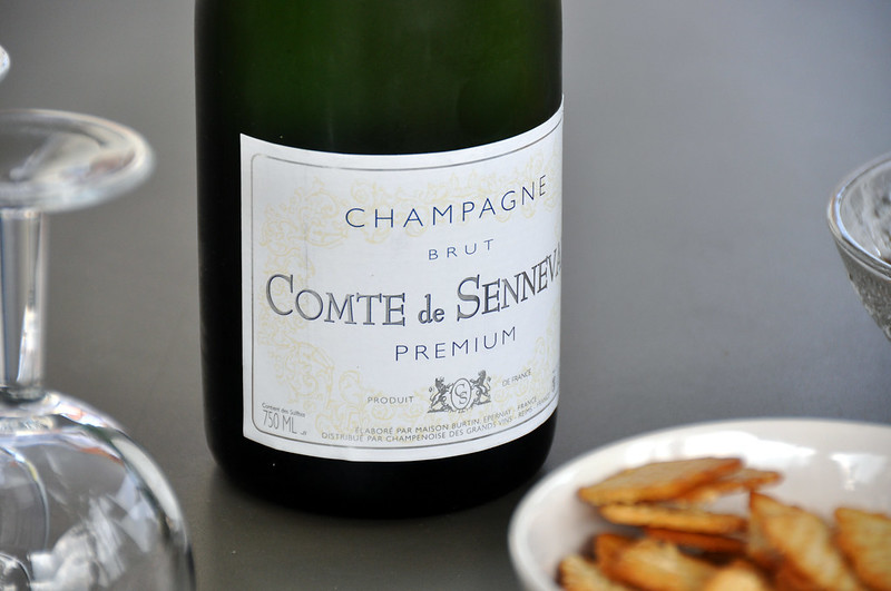 A bottle of Reims champagne sits on a table next to a bowl of crackers.