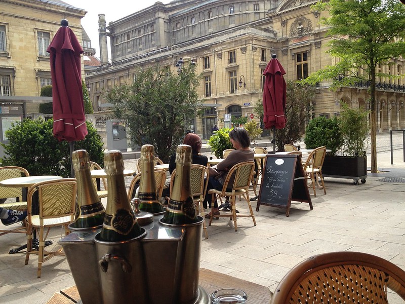 A group of people sitting at a table in Reims with a bottle of wine.