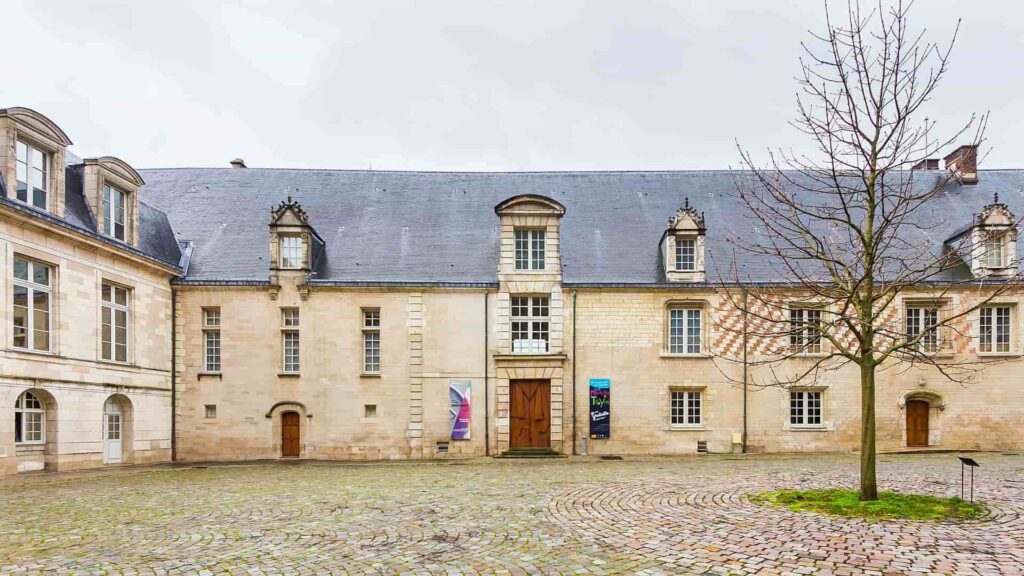 A large stone building with a tree in front of it, located in Troyes.