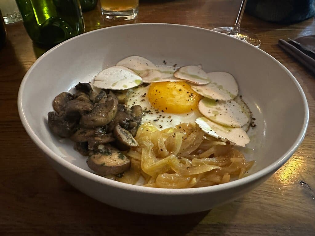 At a Troyes restaurant, a delectable bowl of food is elegantly displayed on a rustic wooden table. The dish features a perfectly cooked egg nestled amidst a medley of earthy