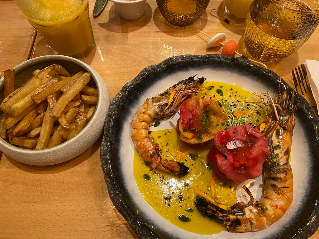 At the charming Troyes Restaurant, indulge in a delectable plate showcasing succulent shrimp accompanied by savory french fries. Enhance your dining experience with a refreshing glass of zesty orange juice.