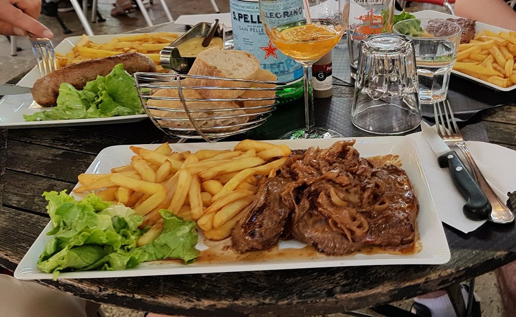 A table at Troyes Restaurant with a plate of steak, fries, and a glass of wine.